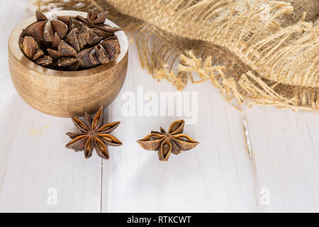 Sacco di intero marrone a secco di anice stellato frutti con ciotola di legno su legno bianco Foto Stock