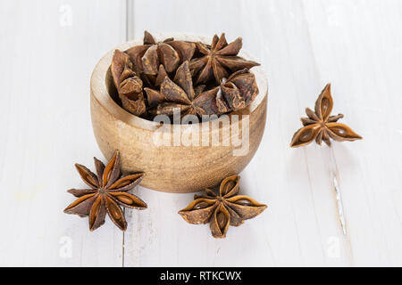 Sacco di intero marrone a secco di anice stellato frutti con ciotola di legno su legno bianco Foto Stock