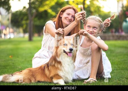 Fun Family - sorridente mamma e figlia e corgi fluffy sedersi sul prato Foto Stock