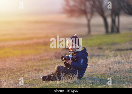 Bambini creativi, kid fotografo (un ragazzino) con una telecamera tenendo il paesaggio immagini nella calda luce del tramonto Foto Stock