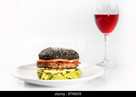 Cheeseburger con pane nero, carni bovine cotoletta, pancetta, pomodori e fette di formaggio e conditi con sugo di pomodoro e insalata verde per un ristorante menu su un bianco è Foto Stock