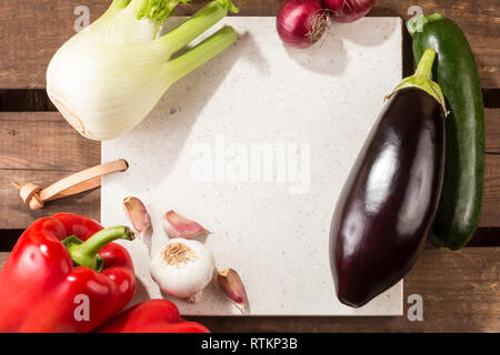 Pietra di calcestruzzo server con spazio per il testo su rustiche tavole di legno. Disposti verdure mediterranee: pepe dolce, finocchio, cipolle, zucchine, melanzane. Foto Stock