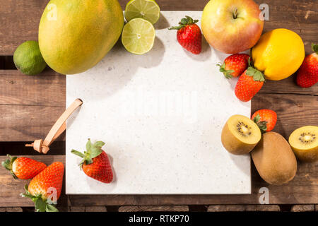 Pietra di calcestruzzo server con spazio per il testo su un legno rustico listone superficie. e disposti frutti. Apple, limone, fragole, kiwi, tigli e mango. Foto Stock
