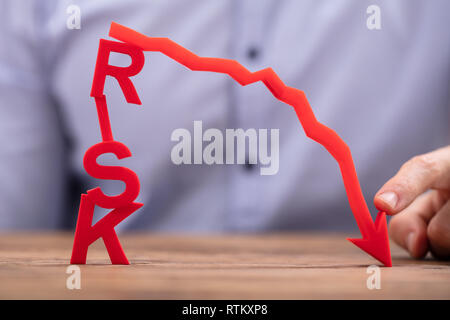 Commercianti di puntamento diminuendo rosso freccia sopra ci rischio testo sulla scrivania in legno Foto Stock