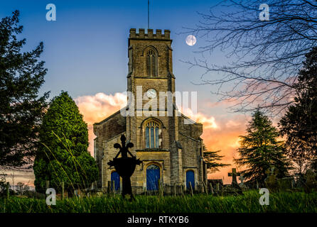 La luna nel cielo di tramonto dietro la chiesa di clock tower in Corsley, Wiltshire, Regno Unito il 20 dicembre 2015 Foto Stock