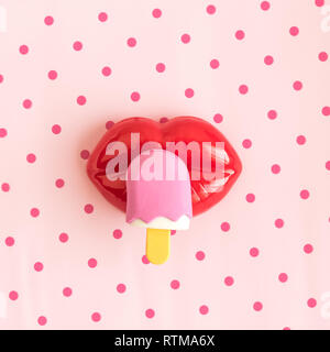 Le labbra con gelato sul bastone contro rosa polka background design minimale cibo creativo e concetti d'estate. Foto Stock