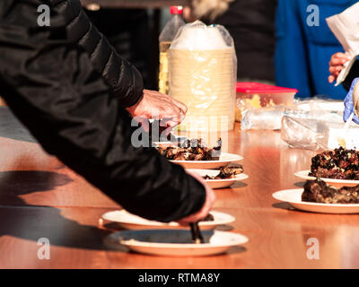Irriconoscibile la persona che ha preso la carne cotta da un piatto di carta in strada a un partito popolare in un villaggio in Spagna Foto Stock