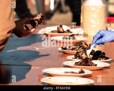 Irriconoscibile la persona che ha preso la carne cotta da un piatto di carta in strada a un partito popolare in un villaggio in Spagna Foto Stock