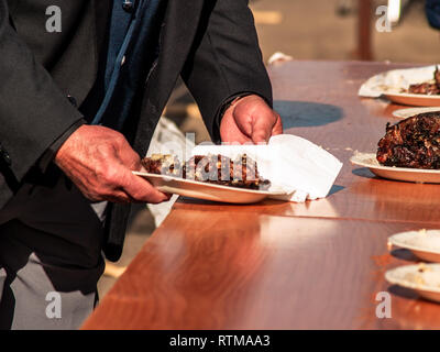 Irriconoscibile la persona che ha preso la carne cotta da un piatto di carta in strada a un partito popolare in un villaggio in Spagna Foto Stock