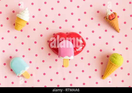 Piatto di laici miniatura gelato e labbra in plastica isolato sul rosa pastello polka background design minimal concetto creativo. Foto Stock