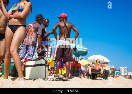 RIO DE JANEIRO - MARZO 15, 2015: un gruppo di unlicensed brasiliano i venditori sulla spiaggia di stare in piedi insieme tra beachgoers sulla riva della spiaggia di Ipanema. Foto Stock