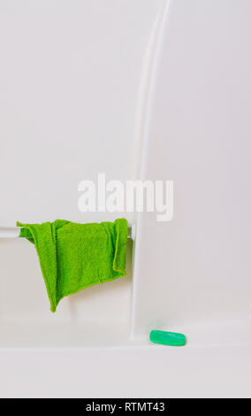 Verticale di close-up shot della parete di una vasca da bagno di colore bianco. Green vestito da corrimano e la barra verde di sapone sul ripiano. Un sacco di spazio copia. Foto Stock