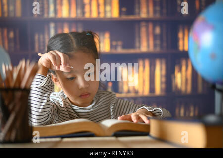 Bambino asiatico ragazza operosa è seduto alla scrivania per interni. Kid è imparare a casa Foto Stock