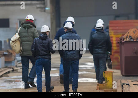 Squadra di lavoratori in bianco caschi passeggiate sul sito in costruzione. Vista posteriore Foto Stock