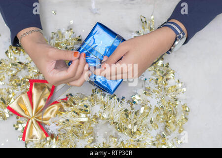 Vista superiore della donna s mani incarto regalo di Natale, close up, impreparato chistmas presenta sulla tavola di cemento a interni home park Foto Stock