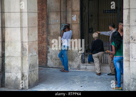 L'Avana, Cuba - 19 Gennaio 2013: una vista delle strade della città con il popolo cubano. Un uomo è al telefono con un telefono a pagamento, altri in attesa. Foto Stock