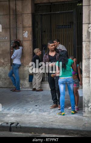 L'Avana, Cuba - 19 Gennaio 2013: una vista delle strade della città con il popolo cubano. Un uomo è al telefono con un telefono a pagamento, altri in attesa. Foto Stock
