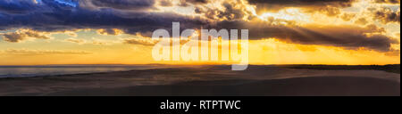 Cloudscape deserta oltre le dune di sabbia di Stockton Beach al tramonto quando il sole basso invia fasci attraverso dense nubi verso il basso ad una ampia fascia di dune tra pac Foto Stock