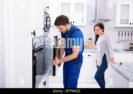 Bella Donna che guarda ai giovani volontari Installazione di forno in cucina Foto Stock