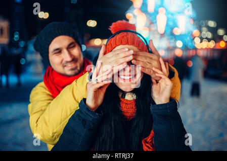 Sera passeggiata invernale, amore giovane gioca indovinare chi sulla piazza. L uomo e la donna avente incontro romantico sulla strada di città con luci Foto Stock