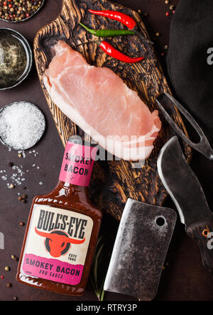 LONDON, Regno Unito - 13 dicembre 2018: Bottiglia di Bull's Eye Smokey barbecue di carne di maiale con salsa di carne di maiale cruda lombatine su vintage tagliere con coltello e forchetta Foto Stock