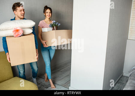 Famiglia giovane giovane acquistato o noleggiato il loro primo piccolo appartamento. Felice gente allegra entrare in camera con scatole di roba. Entusiasti e stupiti Foto Stock