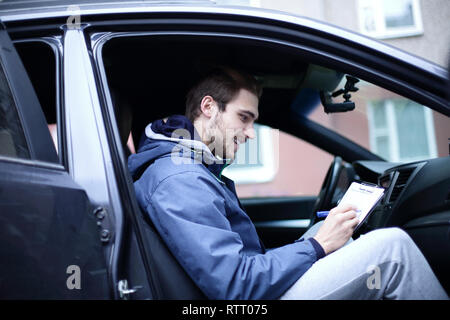 L'uomo firma un documento mentre è seduto in macchina Foto Stock