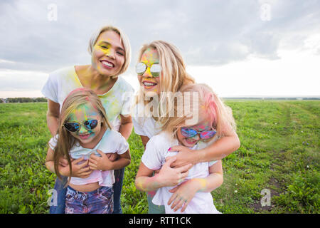 La famiglia, il festival di holi e concetto di vacanze - Close up ritratto di madri e figlie coperto di vernice Foto Stock