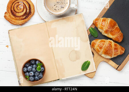 Caffè, cornetti, panini alla cannella e le bacche di prima colazione. Su un tavolo di legno. Vista da sopra con le pagine del libro per il testo Foto Stock