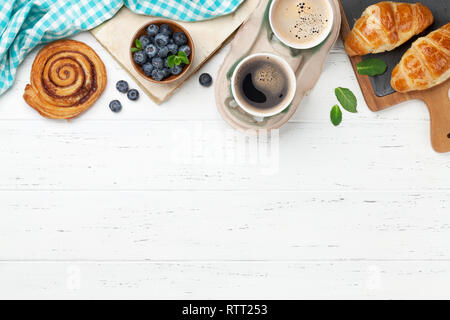 Caffè, cornetti, panini alla cannella e le bacche di prima colazione. Su un tavolo di legno. Vista da sopra con copia spazio per il testo Foto Stock
