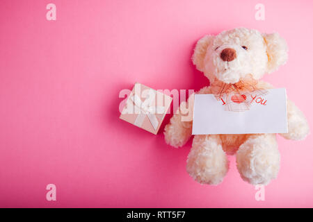 Orsacchiotto di peluche con una confezione regalo e un biglietto per il giorno di San Valentino su sfondo rosa Foto Stock