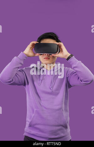 Giovane ragazzo asiatico entusiasmarsi durante la visione di 3 film D utilizzando la realtà virtuale auricolare, posa isolate su viola scuro dello sfondo. Visualiz positivo Foto Stock