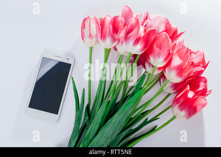 Vista dall'alto di smartphone con bouquet di tulipani rosa su sfondo bianco. Mockup. Piatto, laici spazio copia di cui sopra. Presente per la donna amata Foto Stock