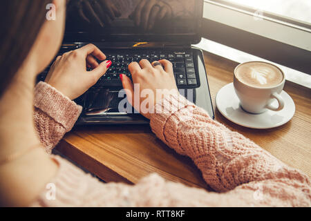 Giovani freelancer gode di caffè nella caffetteria usando un computer portatile nella parte anteriore della finestra Foto Stock