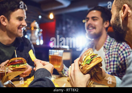 Happy amici mangiare hamburger, bere birra in un bar. Foto Stock