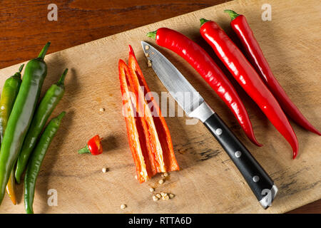 La sgranatura di colore rosso e verde Hot Chili Peppers su una scheda di carving con il coltello Foto Stock