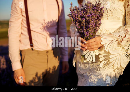 Close-up di un mazzo di fiori di lavanda nelle mani dello sposo e della sposa. Foto Stock