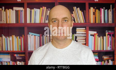 Uomo serio nella libreria. Vista ravvicinata uomo con una testa calva davanti agli scaffali nella libreria ritratto Foto Stock