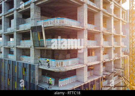 I lavoratori sono l'installazione di elementi prefabbricati di pannello di vetro sul sito in costruzione. Il rivestimento della facciata da una cortina muraria. Foto Stock