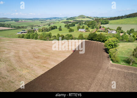 Immagine aerea che mostra le operazioni di aratura di un grande campo da un trattore rosso nella primavera del sole di Clyde Valley area della South Lanarkshire.. Foto Stock