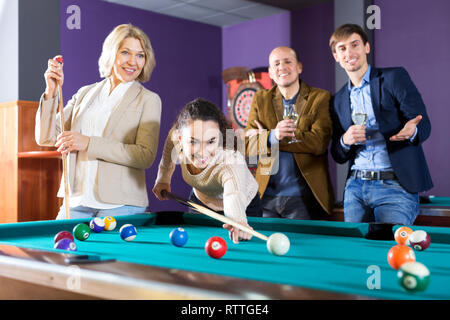 Attraente gruppo di amici a giocare a biliardo e sorridente in un night club. Focus sul giovane donna Foto Stock