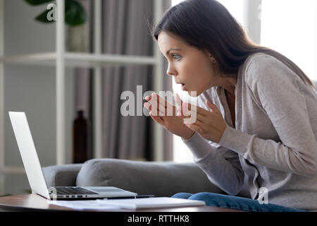 Scioccato donna attraente guardando con stupore lo schermo del notebook Foto Stock