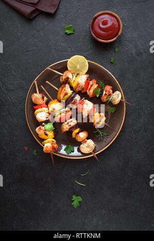 Verdure grigliate e spiedini di pollo con peperoni, zucchine, cipolla e funghi su sfondo nero, vista dall'alto, copia dello spazio. La carne e le verdure Foto Stock