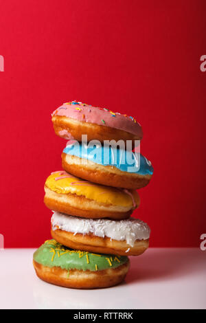 Diverse le ciambelle in multi-smalto colorato impilate una sull'altra su un brillante sfondo rosso con spazio per il testo. Pubblicità panificio concetto. Hanukka Foto Stock