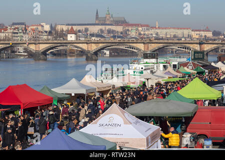 Praga, Repubblica Ceca - 16 febbraio 2019: Persone e si trova presso il mercato degli agricoltori a Naplavka riverbank, con i ponti e il Castello di Praga in b Foto Stock