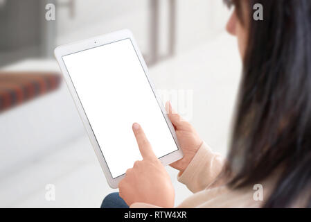 Donna utilizzare bianco tablet con schermo isolata forma mockup, app o la presentazione del sito web. Vista sulla spalla. Home interno in background. Foto Stock