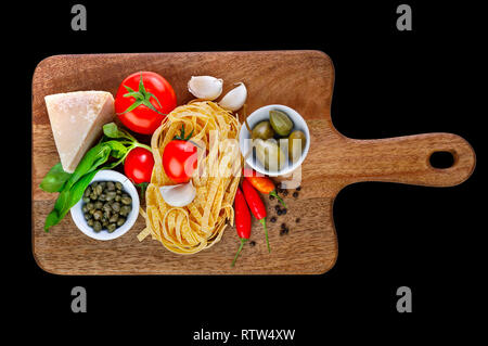 Parmigiano, capperi, pomodoro, aglio, basilico, peperoncino paprica, pepe e tagliatelle sul tagliere di legno isolato su sfondo nero. Ingredienti Foto Stock