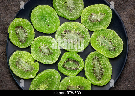 Fette di essiccato kiwi su una piastra nera contro textured fatti a mano carta di corteccia Foto Stock