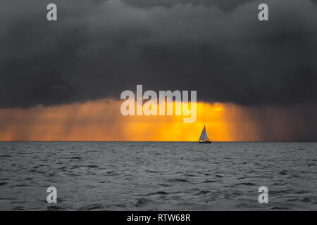 Lonely barca a vela in oceano di fronte di tempesta in avvicinamento e scure nuvole basse con una luce di sunrise, canale inglese, vicino alla Francia Foto Stock