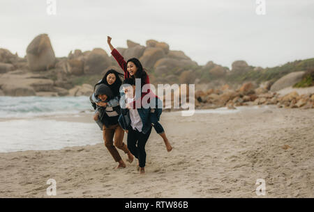 Due giovani uomini dando loro fidanzate piggyback giostre. Un gruppo di giovani che si diverte durante il periodo estivo presso la spiaggia. Foto Stock